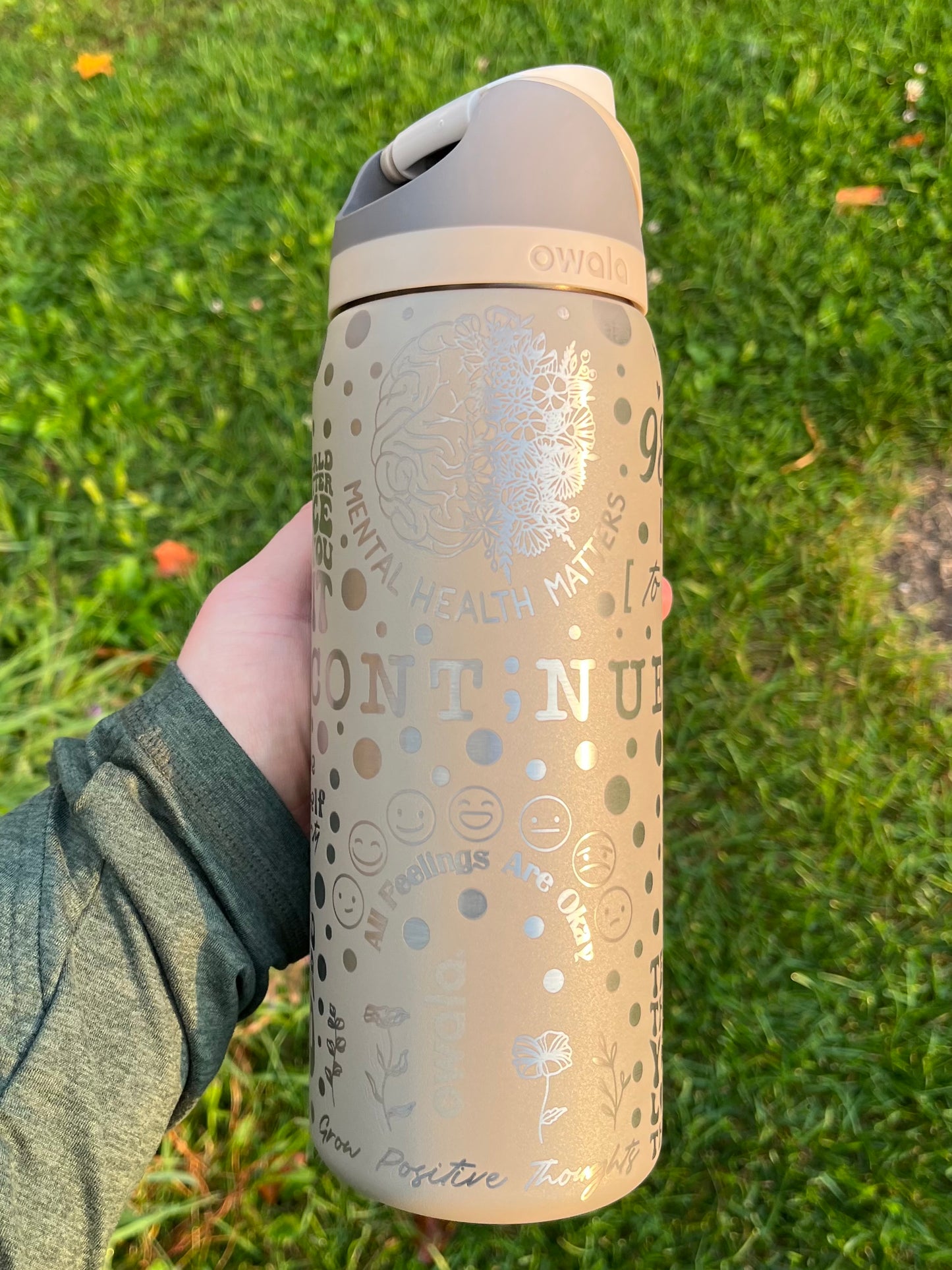 Beige water bottle with motivational text held in a hand on grass