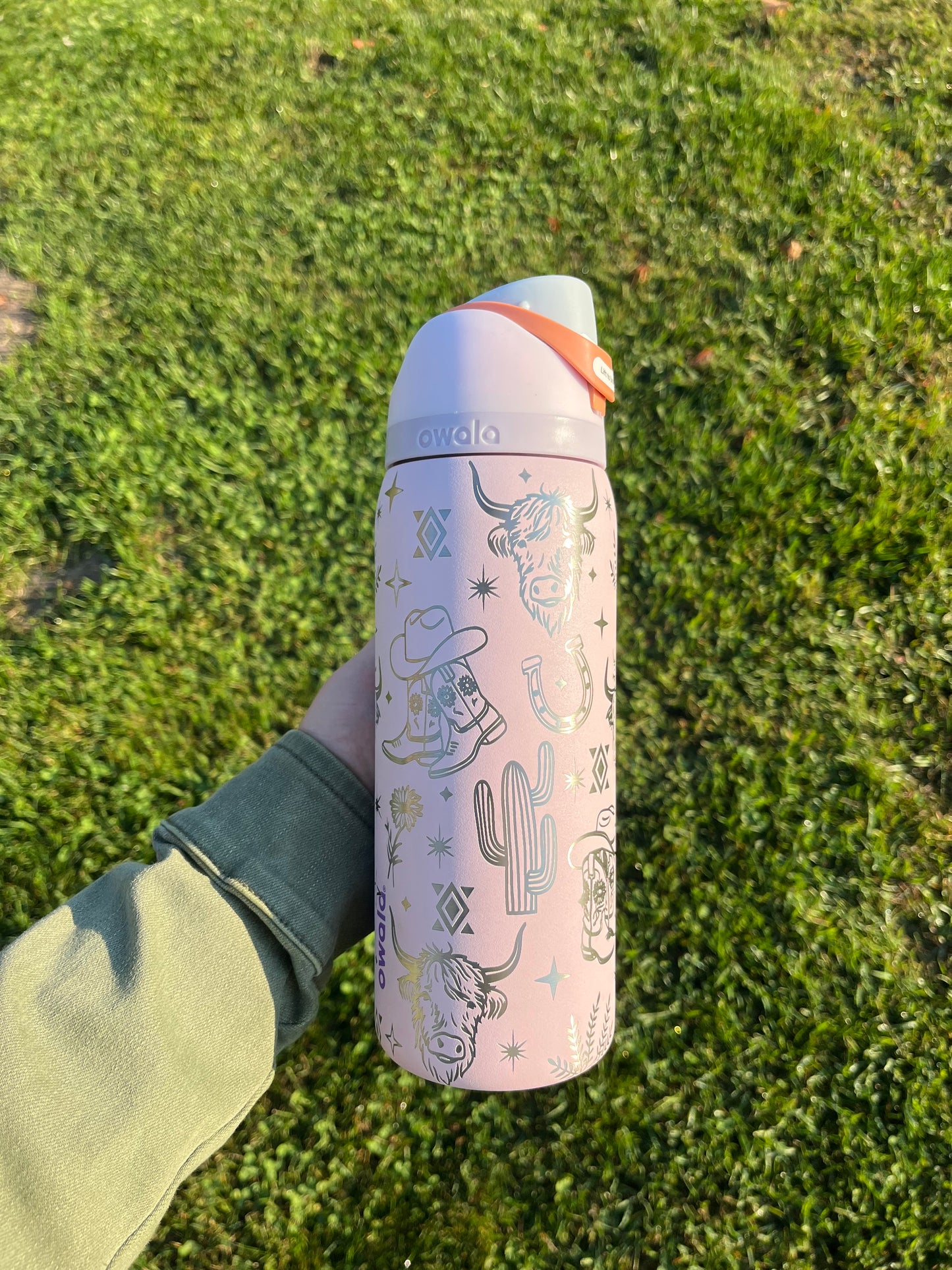 Person holding a pink thermos with cactus design on grass