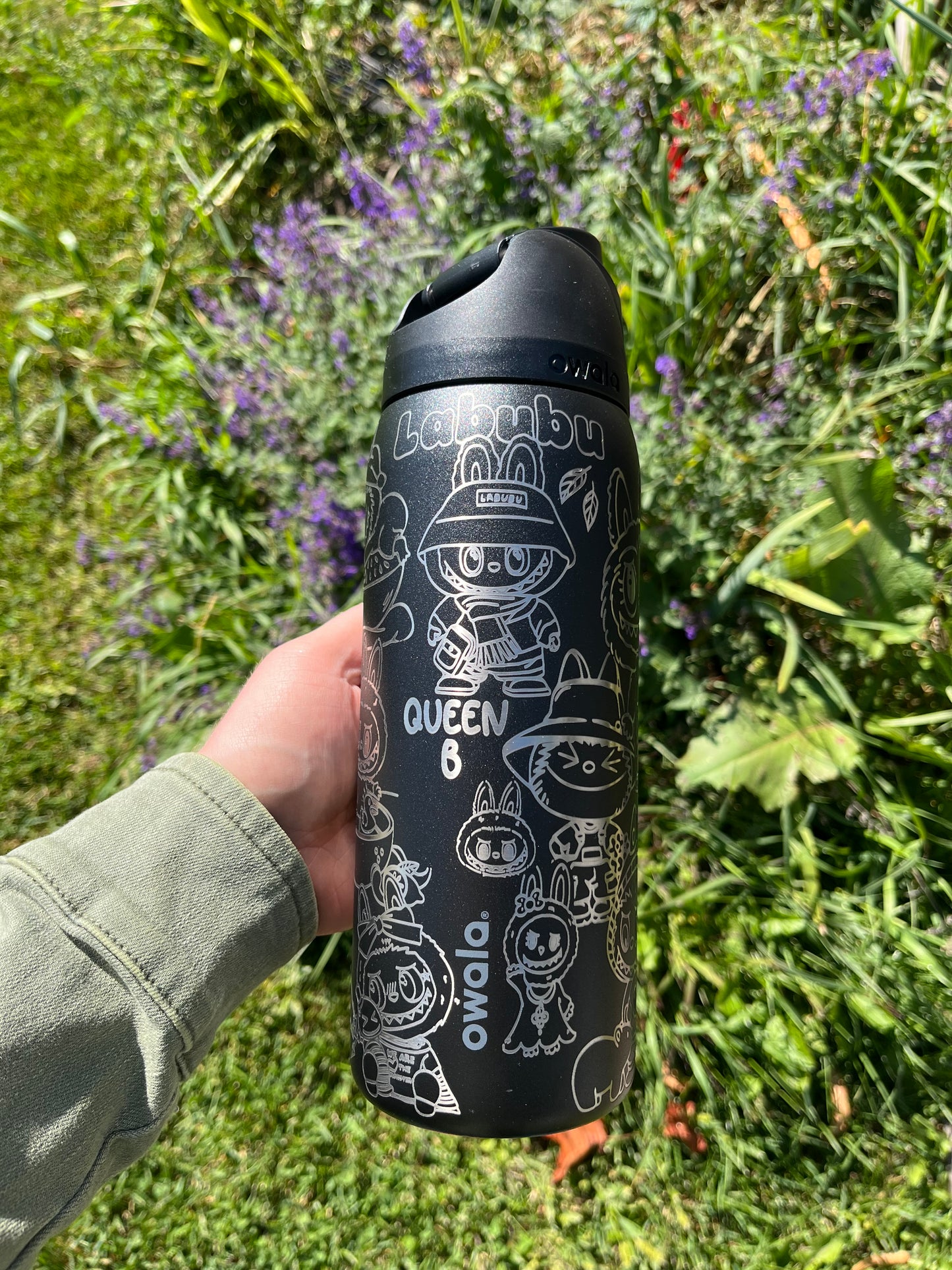 Black travel mug with white designs held in front of a grassy background