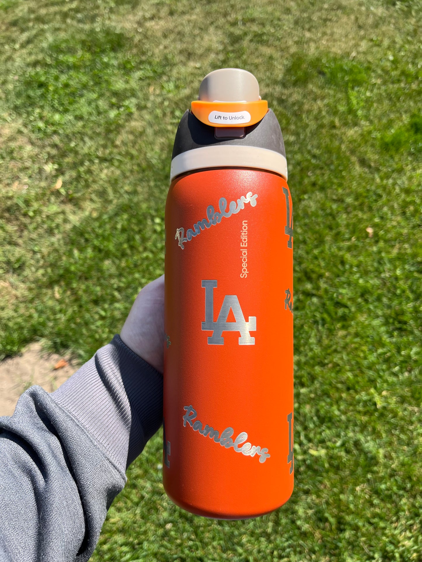 Person holding an orange water bottle with 'Los Angeles' branding against a grassy background