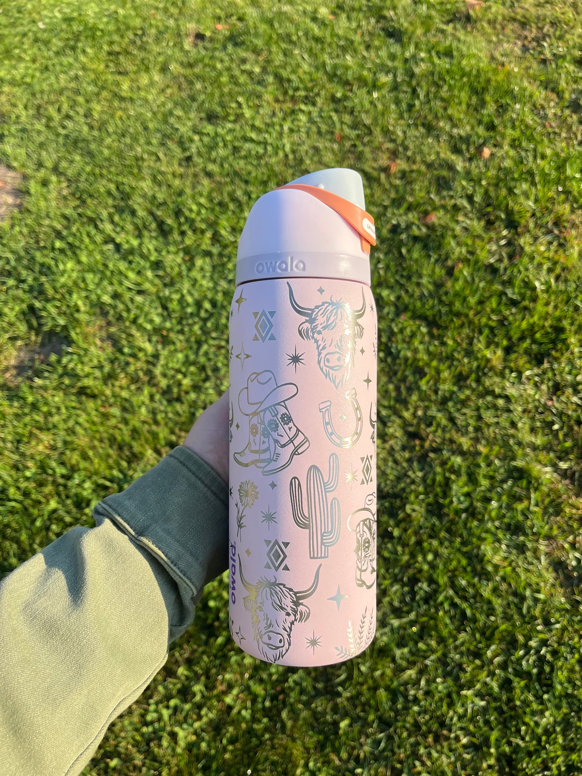 Person holding a pink thermos with cactus design on grass