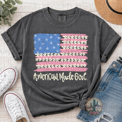 Comfort Colors 1717 pepper gray t-shirt featuring a distressed American flag design with daisy flowers and “American Made Girl” text in cream lettering.