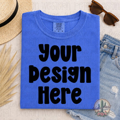 Comfort Colors Flo Blue blank t-shirt mockup in a styled summer flat lay with denim shorts, sunglasses, straw hat, and neutral beach-inspired accessories.