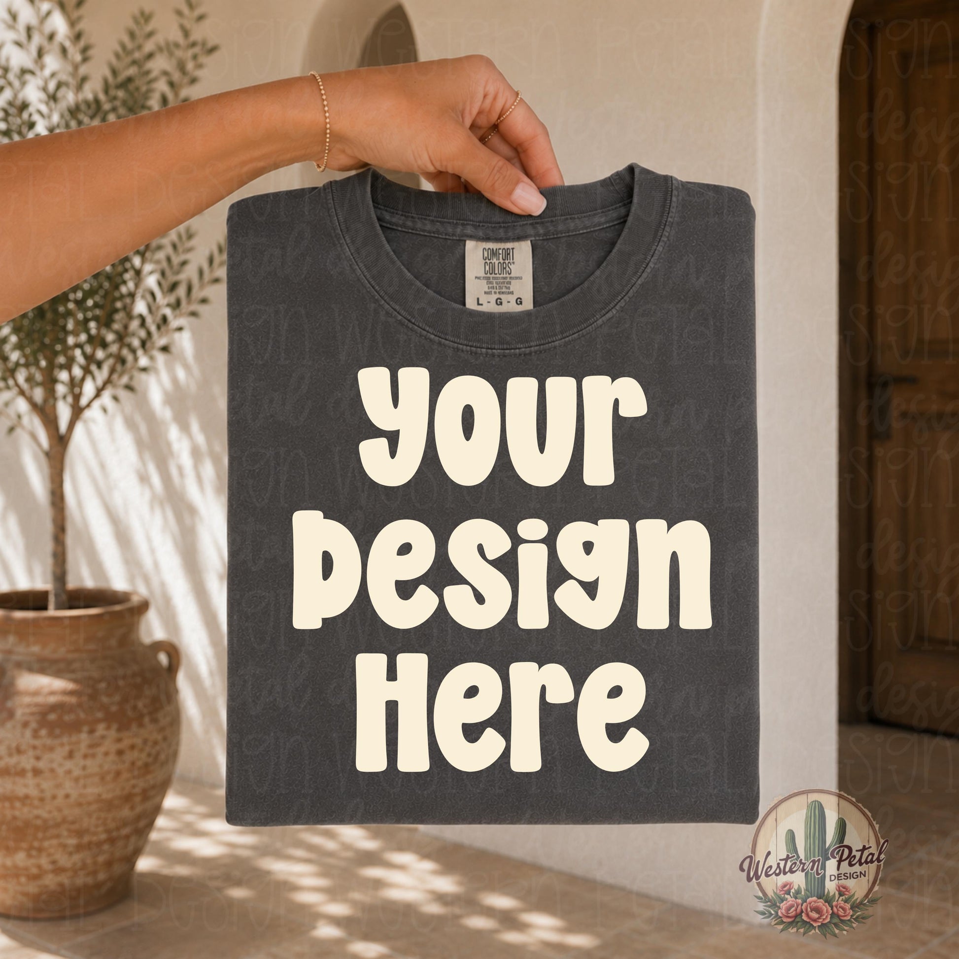 Hand holding a folded Comfort Colors pepper t shirt mockup in a warm neutral boho setting with aesthetic boutique styling and soft natural lighting.