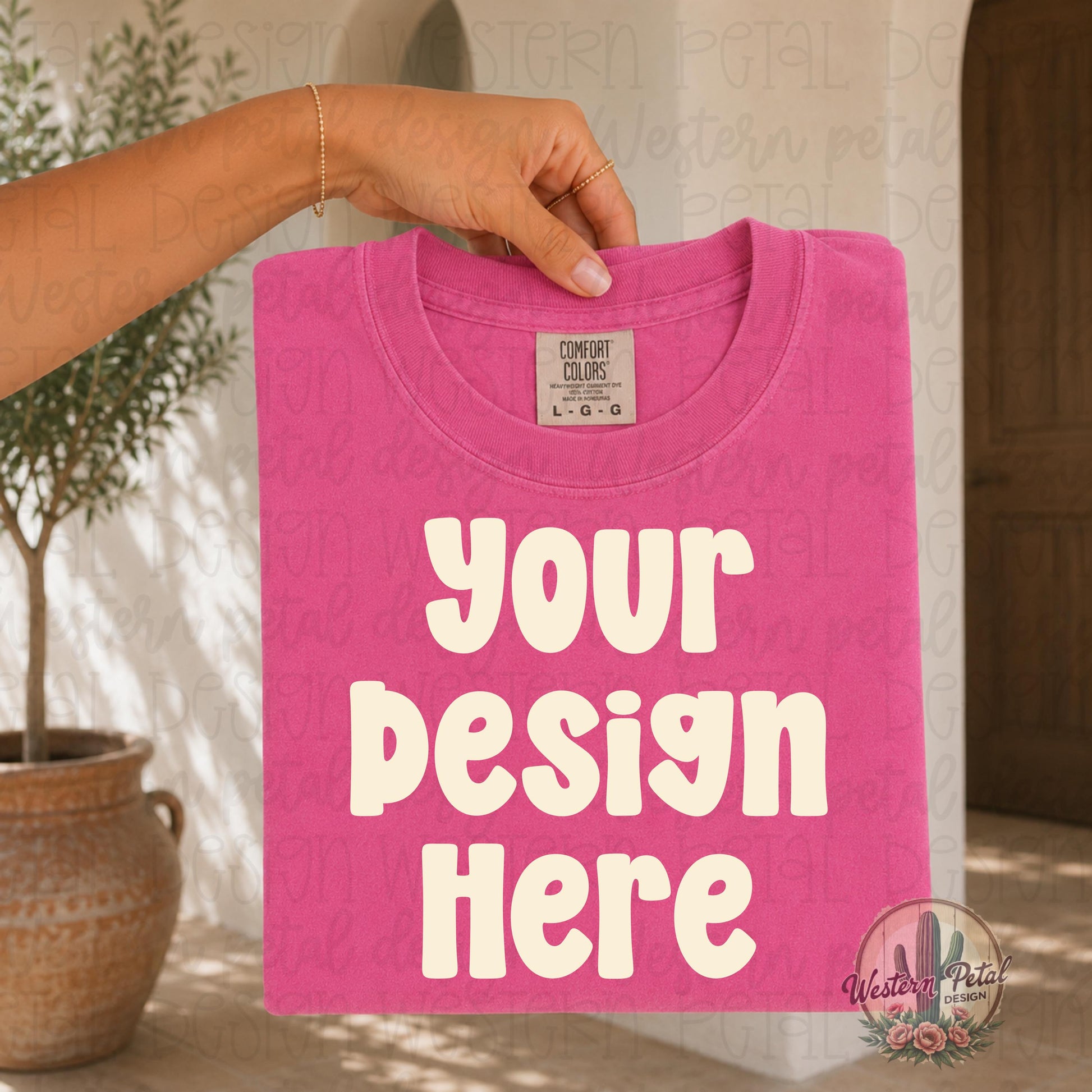 Hand holding a folded Comfort Colors crunchberry pink t shirt mockup in a warm neutral boho setting with boutique aesthetic styling and natural lighting.