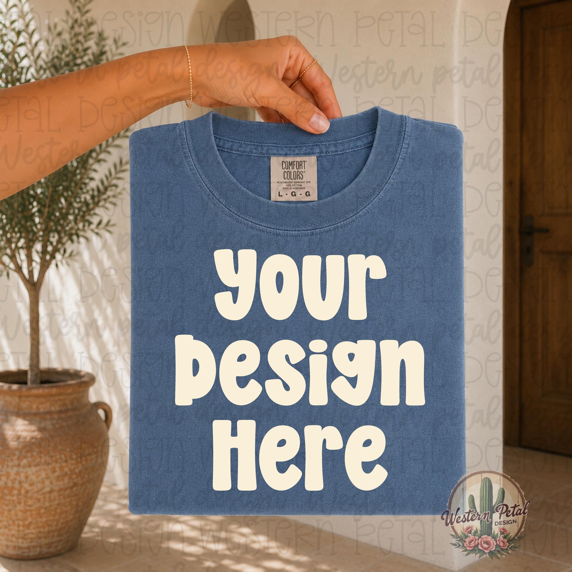 Hand holding a folded Comfort Colors blue jean t shirt mockup in a warm boho styled setting with neutral earthy tones and natural lighting.