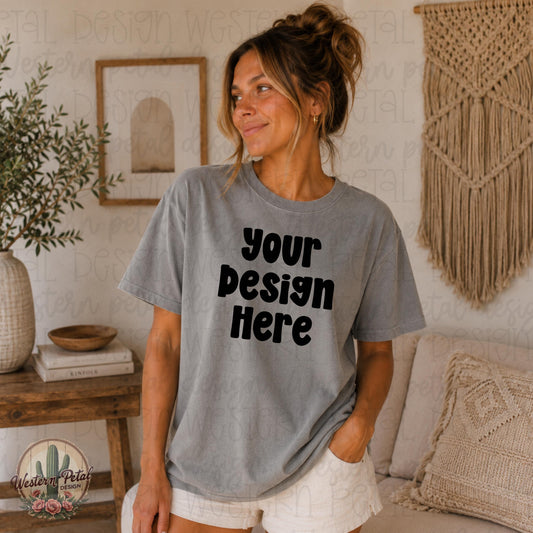Cozy boho Comfort Colors grey mockup featuring a brunette model with a messy bun wearing an oversized grey t-shirt in a warm neutral indoor setting with macrame decor and earthy textures.