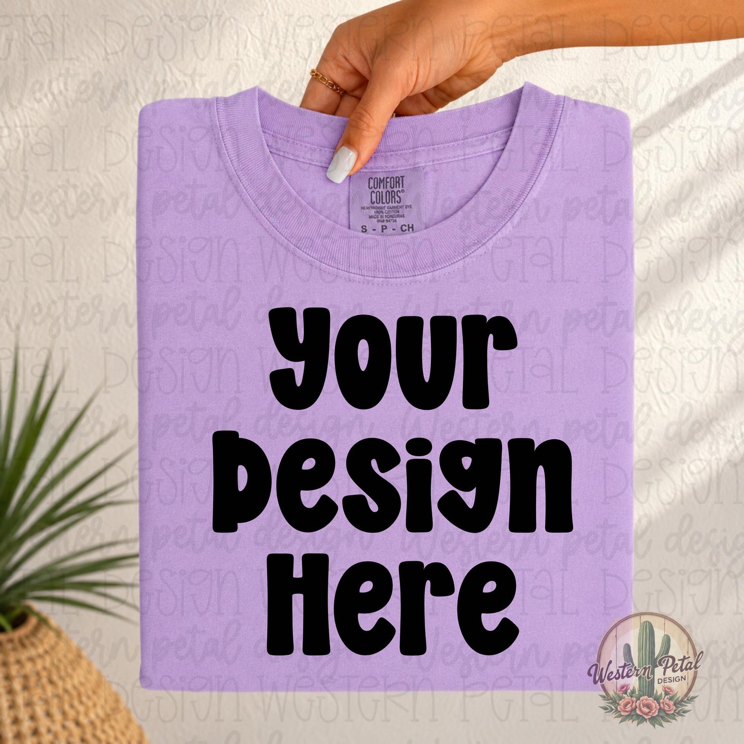 Folded orchid Comfort Colors t-shirt mockup held from the top by a woman’s hand with neutral nails in a soft boho western setting.