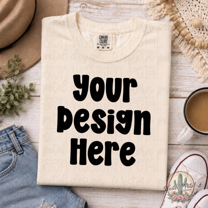 Blank Comfort Colors 1717 ivory t-shirt mockup folded on white wood background with coffee mug, denim jeans, sneakers, greenery, and neutral boho accessories.