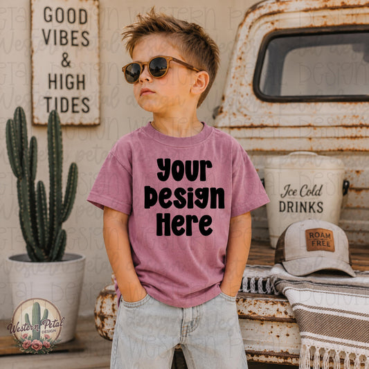 Little boy wearing a mauvelous Rabbit Skins t-shirt mockup standing in front of a vintage truck with western summer decor and sunglasses.