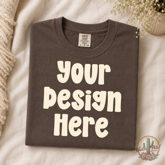 Folded espresso brown Comfort Colors shirt mockup styled on cream bedding with neutral boho decor and soft feminine aesthetic