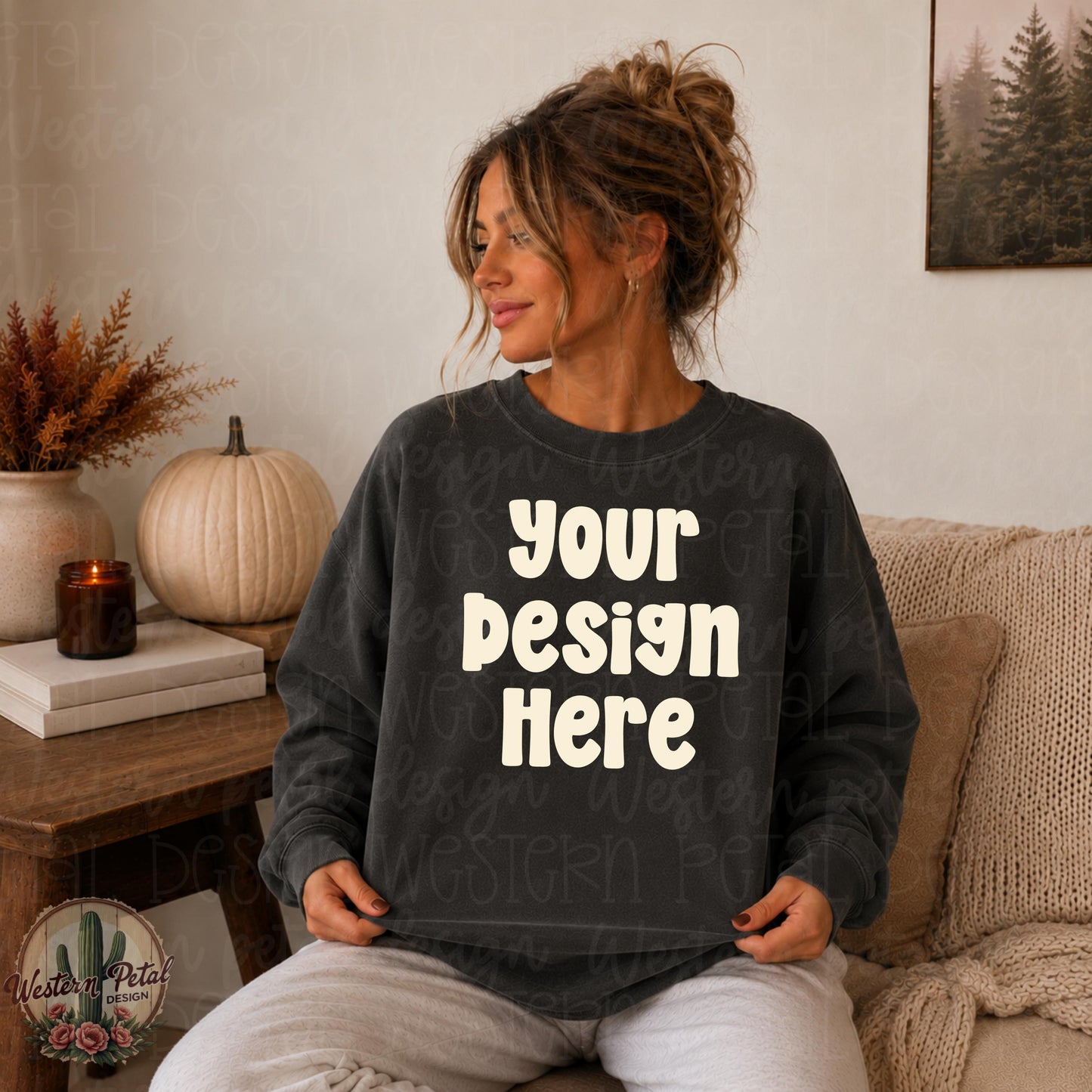 Woman with messy bun wearing a pepper Comfort Colors 1566 crewneck sweatshirt in a cozy neutral fall living room, holding sweatshirt flat for mockup display.