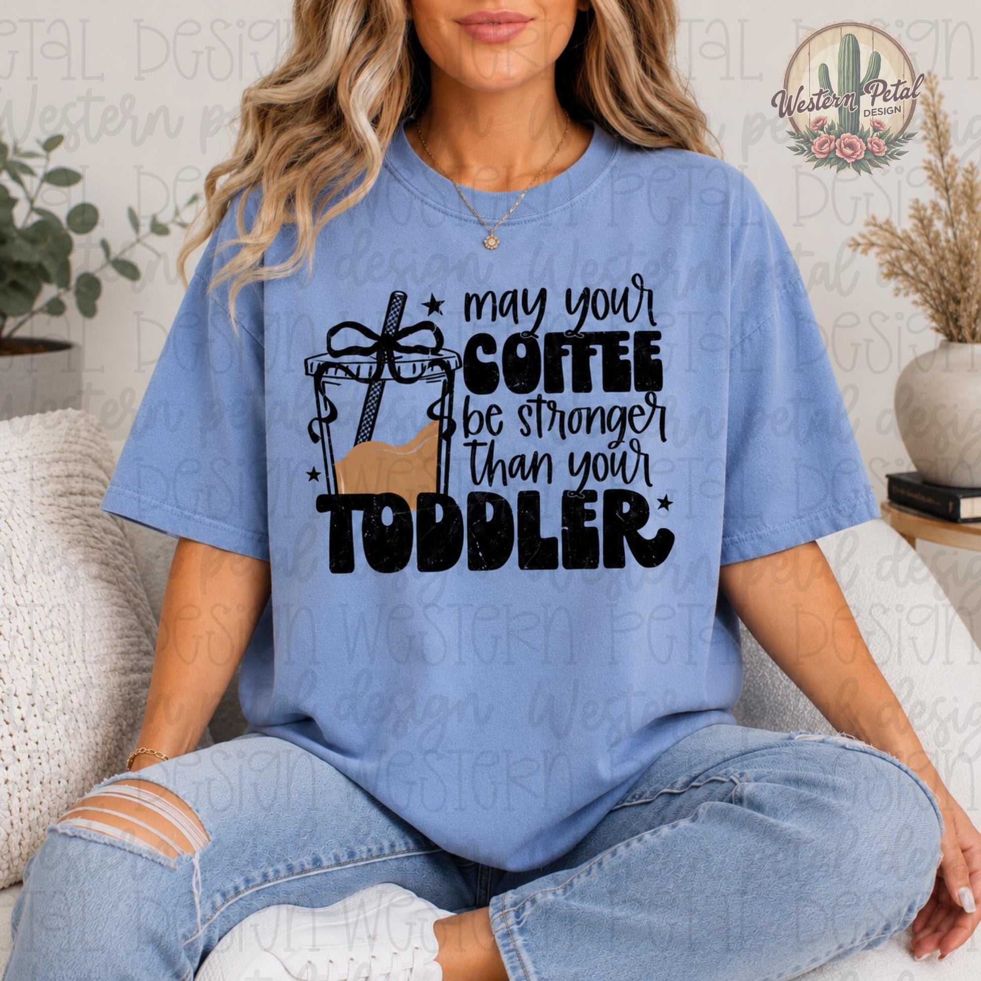 Woman wearing a Comfort Colors 1717 t-shirt with “May Your Coffee Be Stronger Than Your Toddler” graphic in blue denim color.