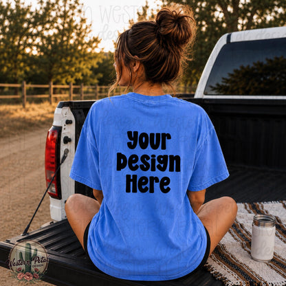 Woman sitting in the back of a pickup truck wearing a Comfort Colors 1717 flo blue shirt mockup with oversized back design placement and trendy western outdoor vibe.