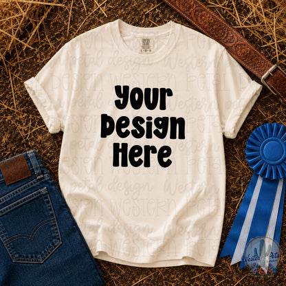 Comfort Colors 1717 Ivory t-shirt flat lay mockup with blue ribbon, western tooled leather belt, denim jeans, and livestock show themed background.